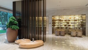 A modern lobby with a large potted plant, a wooden bench, and a seating area with tables and chairs. - Ji Hotel (Huzhou)