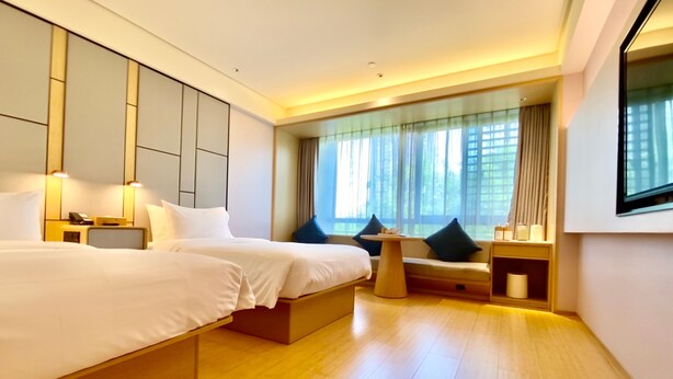 A hotel room with two beds, a small table, a sofa, and a large window with curtains. - Ji Hotel (Huzhou)