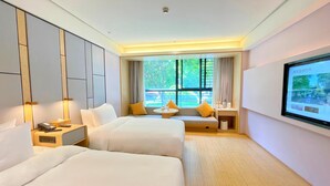 A hotel room with two beds, a bedside table with a phone, a small table with a lamp, and a TV screen displaying a landscape. - Ji Hotel (Huzhou)