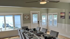 Comedor con una larga mesa dispuesta para seis personas, ventanas amplias con vistas y un ventilador de techo.