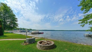 Un parque junto al lago con un área para fogatas, un muelle con barcos y una zona verde.