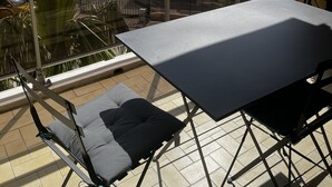 Ein Balkon mit Tisch und Stühlen, der auf einen Parkplatz und ein mehrgeschossiges Gebäude blickt.