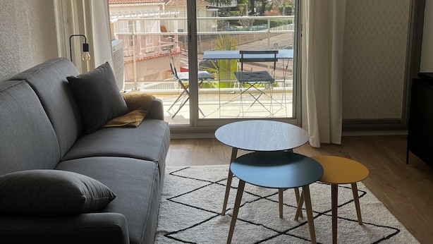 Ein modernes Wohnzimmer mit einem grauen Sofa, einem kleinen runden Tisch und einem gemusterten Teppich.