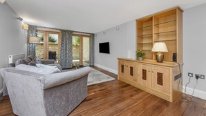 Una sala de estar con un sofá gris, un mueble de madera y un televisor en la pared.