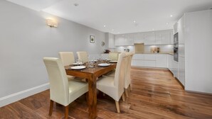 Un comedor moderno con una mesa de madera dispuesta para seis personas, rodeada de sillas blancas tapizadas.