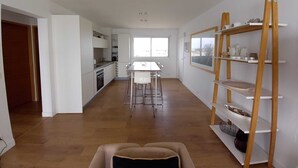 A modern kitchen with white cabinets, a dining area with a white table and chairs, and a wooden shelf unit against the wall. - WATERFRONT APARTMENT FACING THE SEA (Agde)