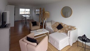 A spacious living area with a sofa, armchair, and coffee table. A dining area with chairs and a table is visible in the background. - WATERFRONT APARTMENT FACING THE SEA (Agde)