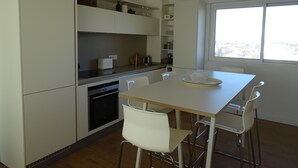 A modern kitchen with white cabinetry, a built-in oven, and a dining area with a white table and chairs. - WATERFRONT APARTMENT FACING THE SEA (Agde)