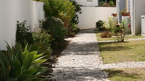 A narrow cobblestone pathway flanked by lush greenery and potted plants, leading to a white building with a door. - Holiday house with big roof terrace pool and sea view (Porches,Lagoa)