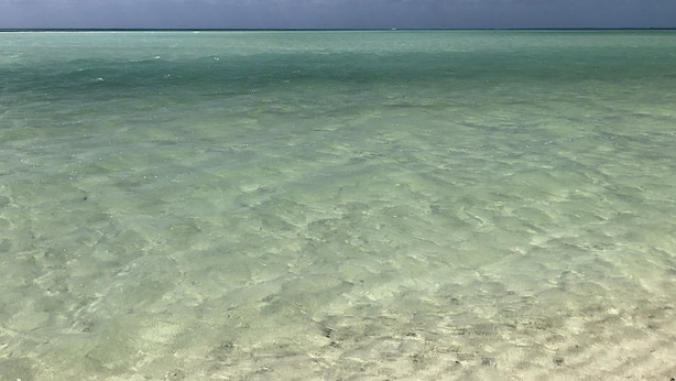 A clear view of a beach with turquoise water and a blue sky with scattered clouds.