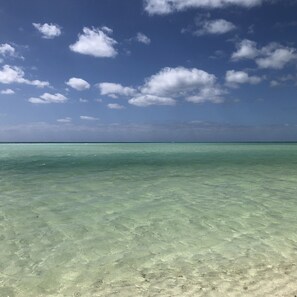 A clear view of a beach with turquoise water and a blue sky with scattered clouds.