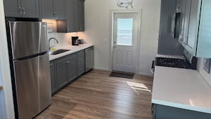 A modern kitchen with grey cabinets, stainless steel appliances, and a wooden ceiling.