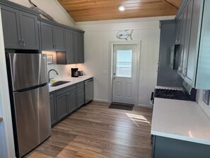 A modern kitchen with grey cabinets, stainless steel appliances, and a wooden ceiling.