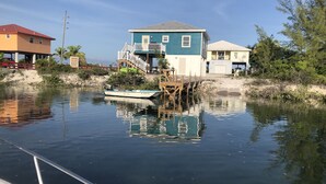 A house with a dock extending into a calm body of water, surrounded by vegetation and other houses.