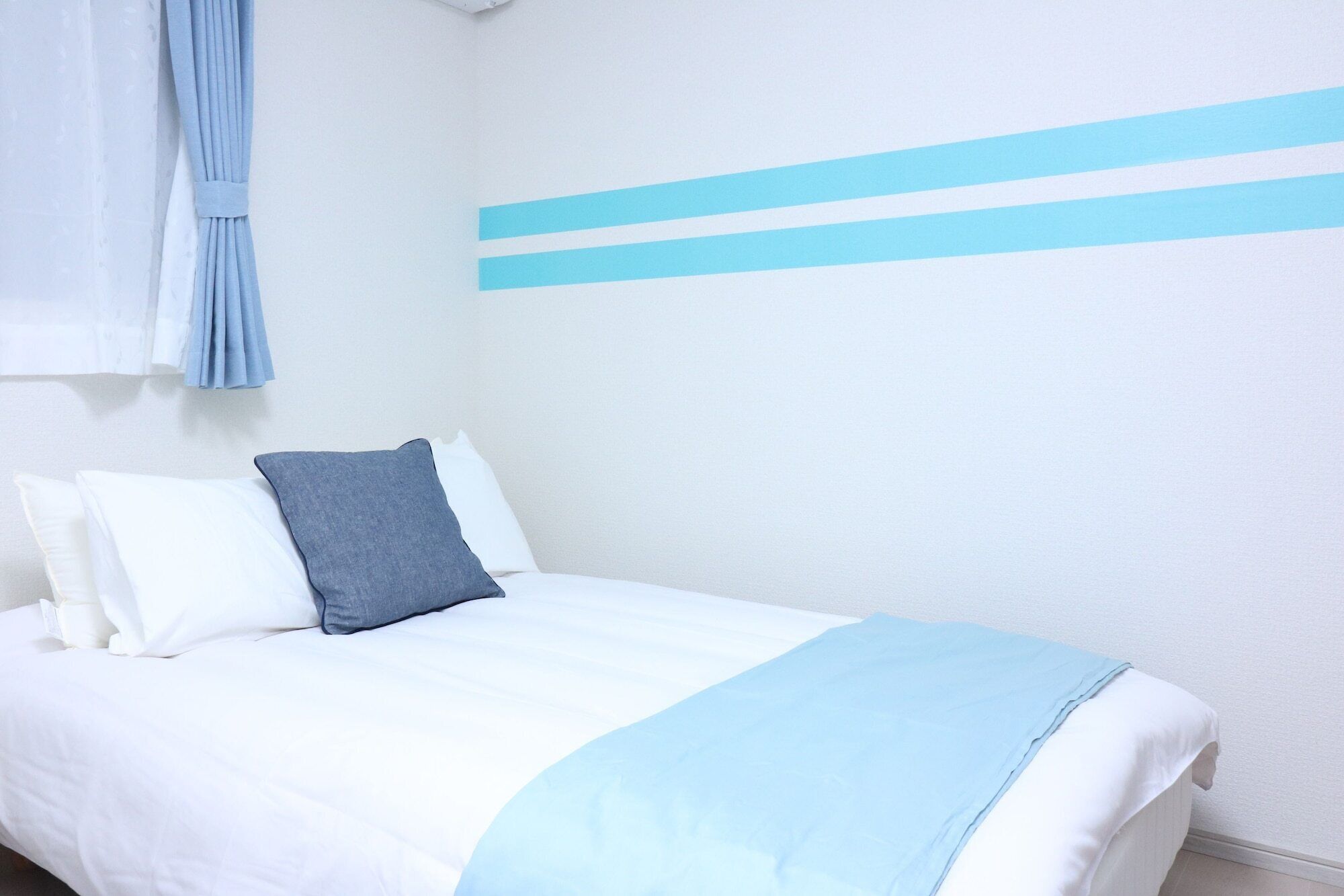 A bed with white and blue bedding, a grey pillow, and a blue blanket.