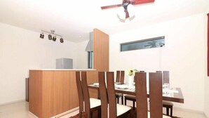 A modern dining area with a wooden table, dark chairs, a brown rug, and a ceiling fan. - HG Cozy Hotel (Neyagawa)