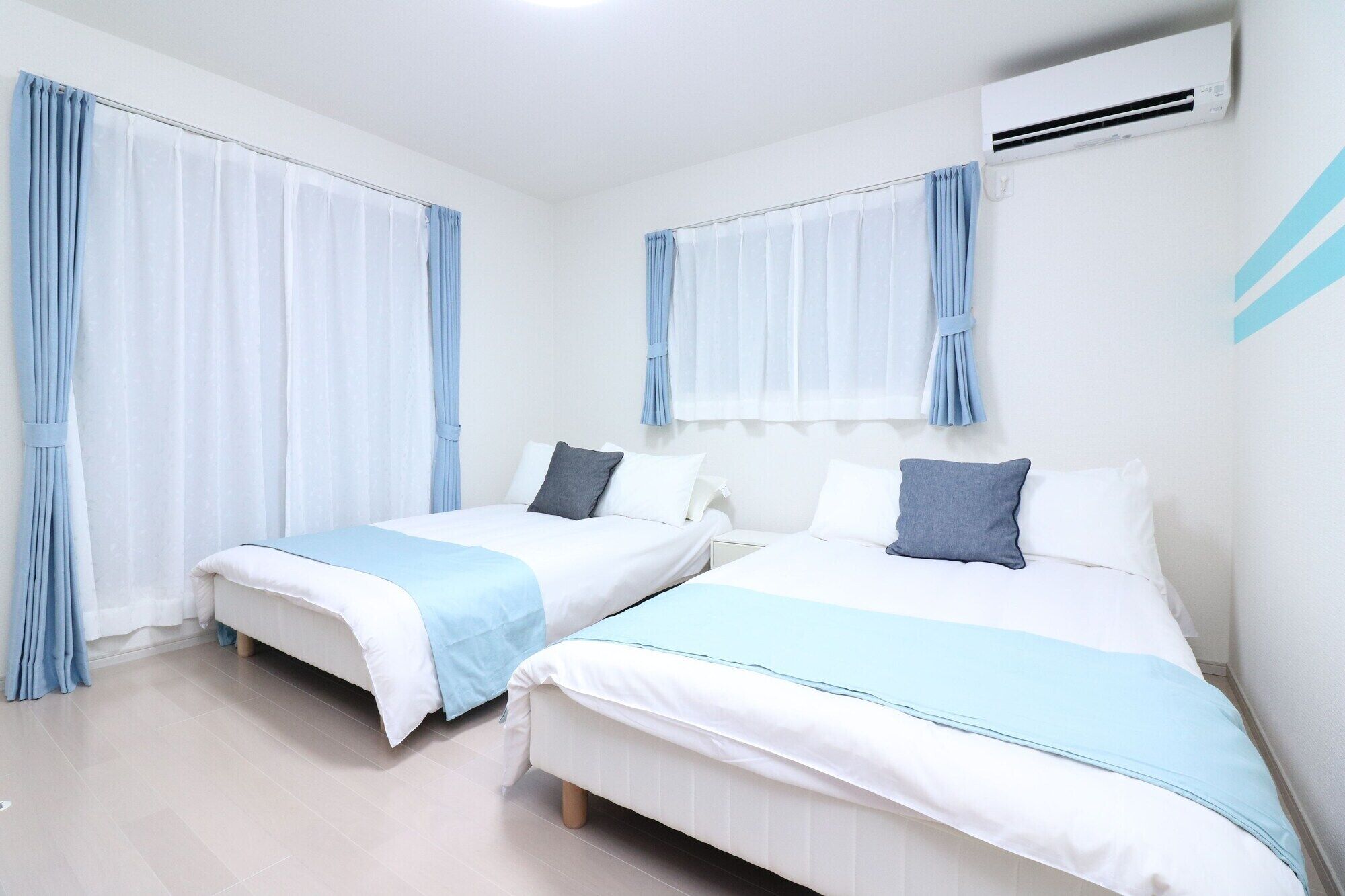A hotel room with two beds, each with a blue and white bedspread, and light blue curtains.