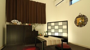 A small room with a desk, two chairs, a cabinet, a window with brown curtains, and a wall-mounted decorative panel. - HG Cozy Hotel (Neyagawa)