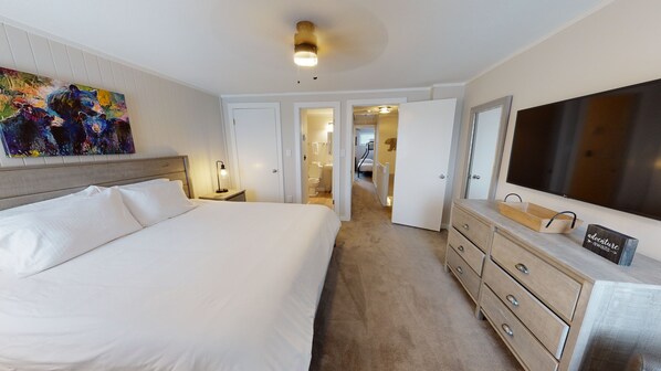 A hotel room with a large bed, a dresser, a TV, and a painting on the wall.