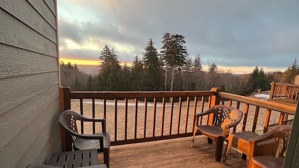 Une terrasse en bois, dotée de mobilier d’extérieur, et offrant une vue sur les arbres et le coucher du soleil.