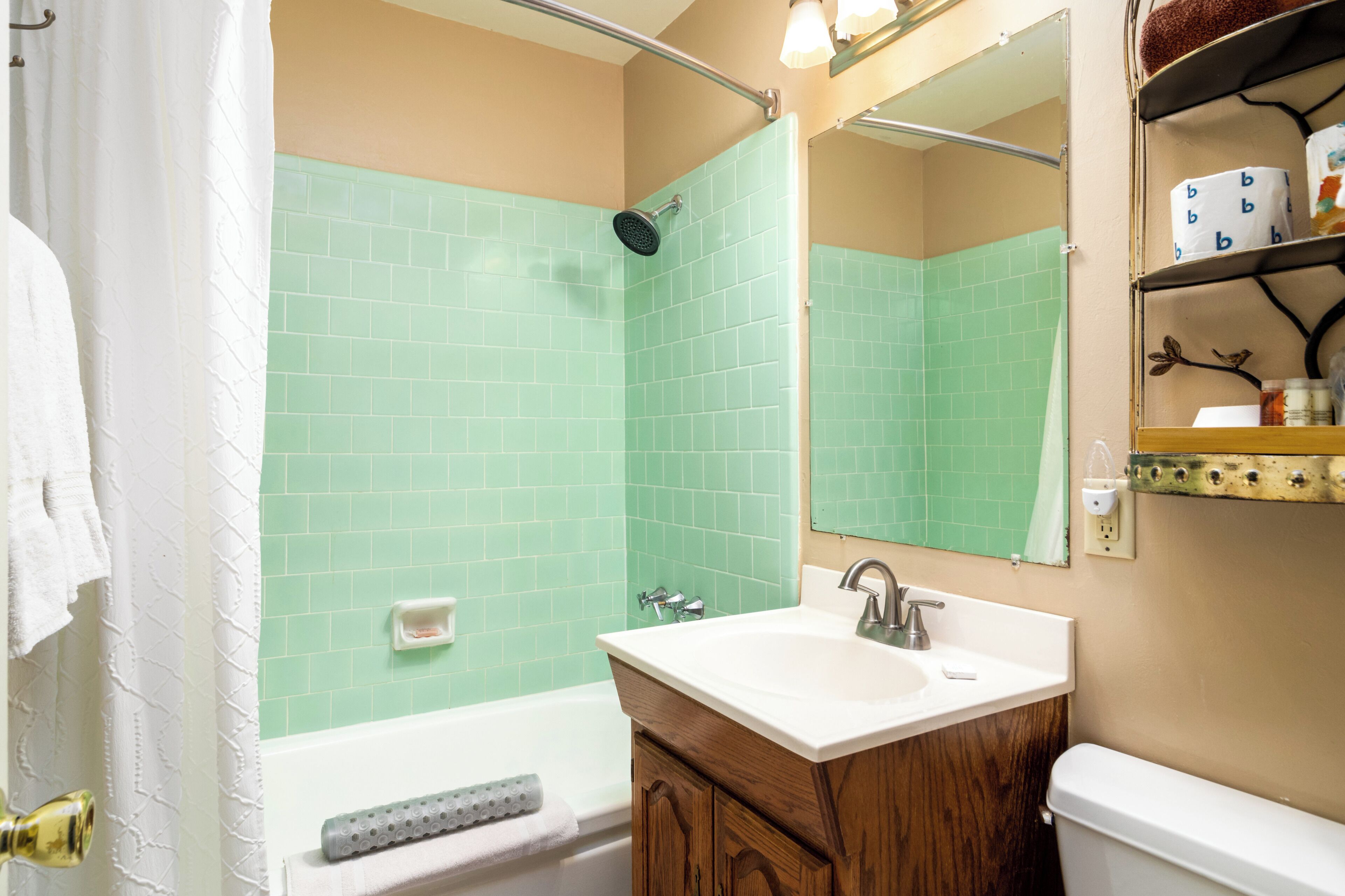 A bathroom with a green-tiled shower, a white sink, wooden cabinets, and a mirror above the sink.