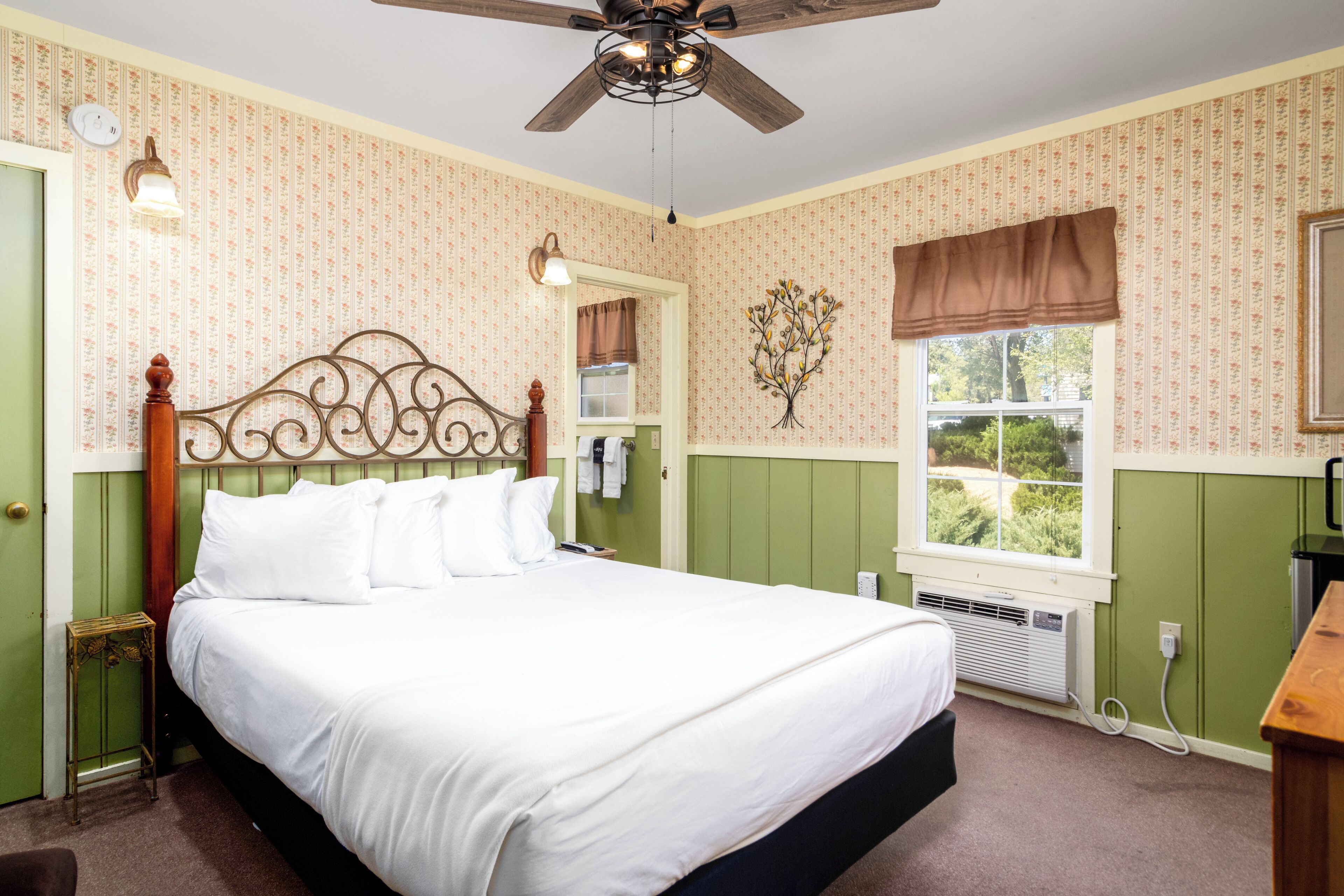 Une chambre avec un grand lit, un ventilateur de plafond, une fenêtre donnant sur un beau paysage et des murs verts.