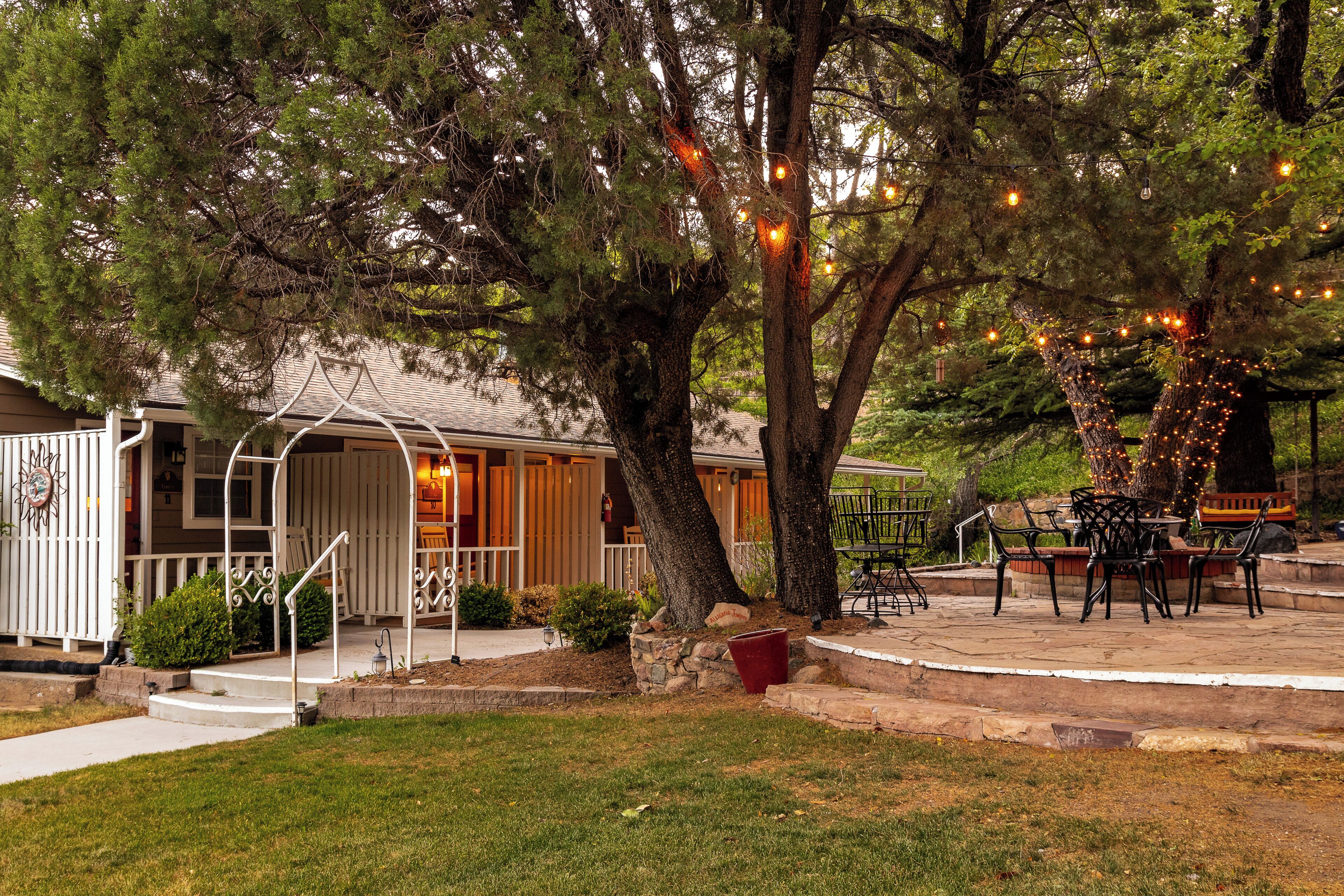 A covered outdoor patio with a stone bench and table, surrounded by trees and a house with a porch.