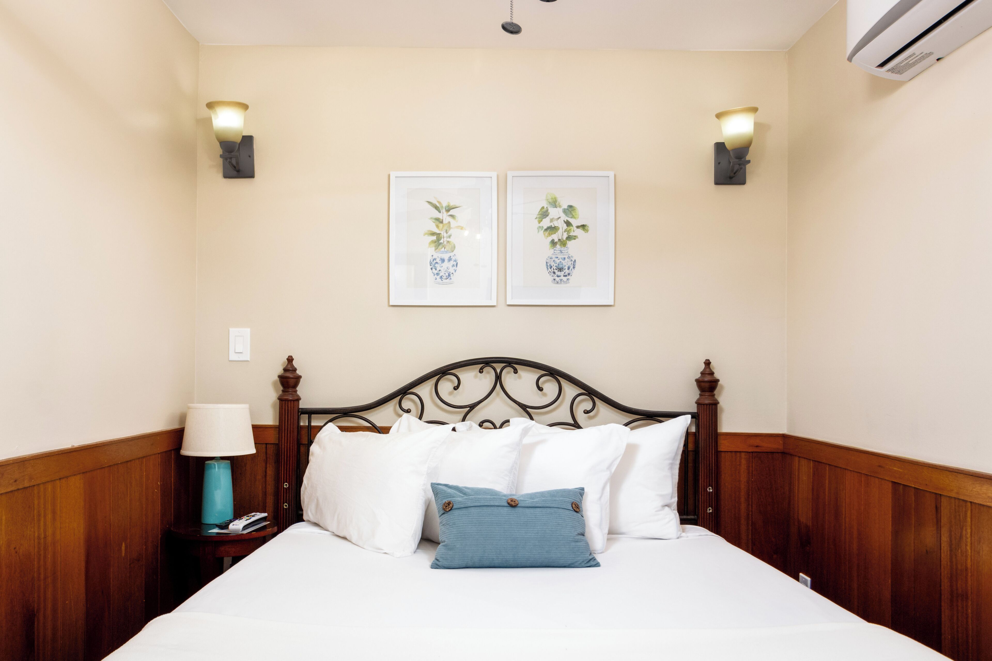 Un letto rifatto con cuscini bianchi e blu, una testiera in legno e due applique.