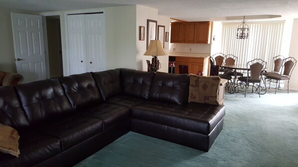 Ein Wohnzimmer mit einem dunkelgrauen Ledersofa, einem Essbereich mit Metallstühlen und einer Küche mit Holzschränken.