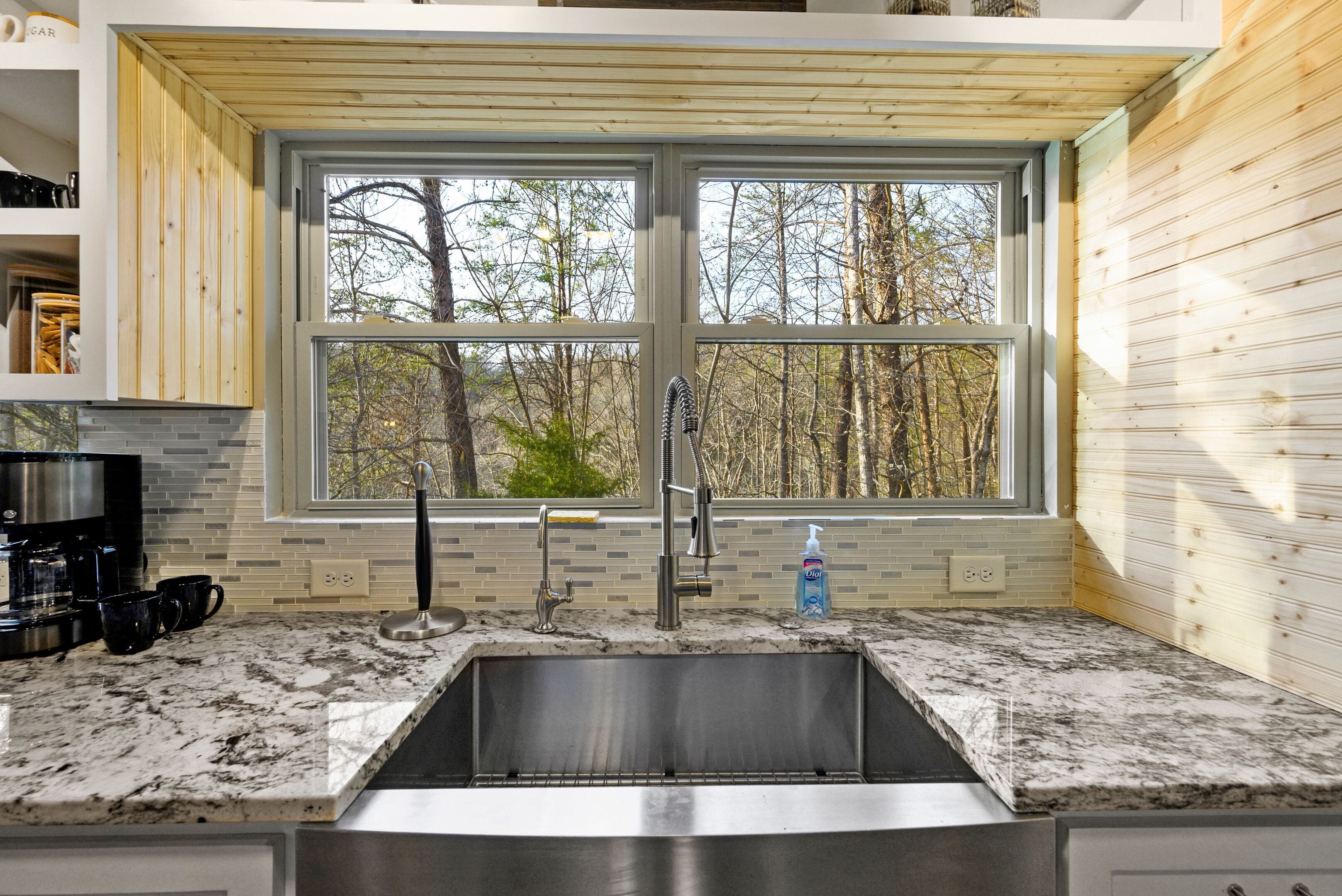 A kitchen with a large window, a stainless steel sink, and a marble countertop.