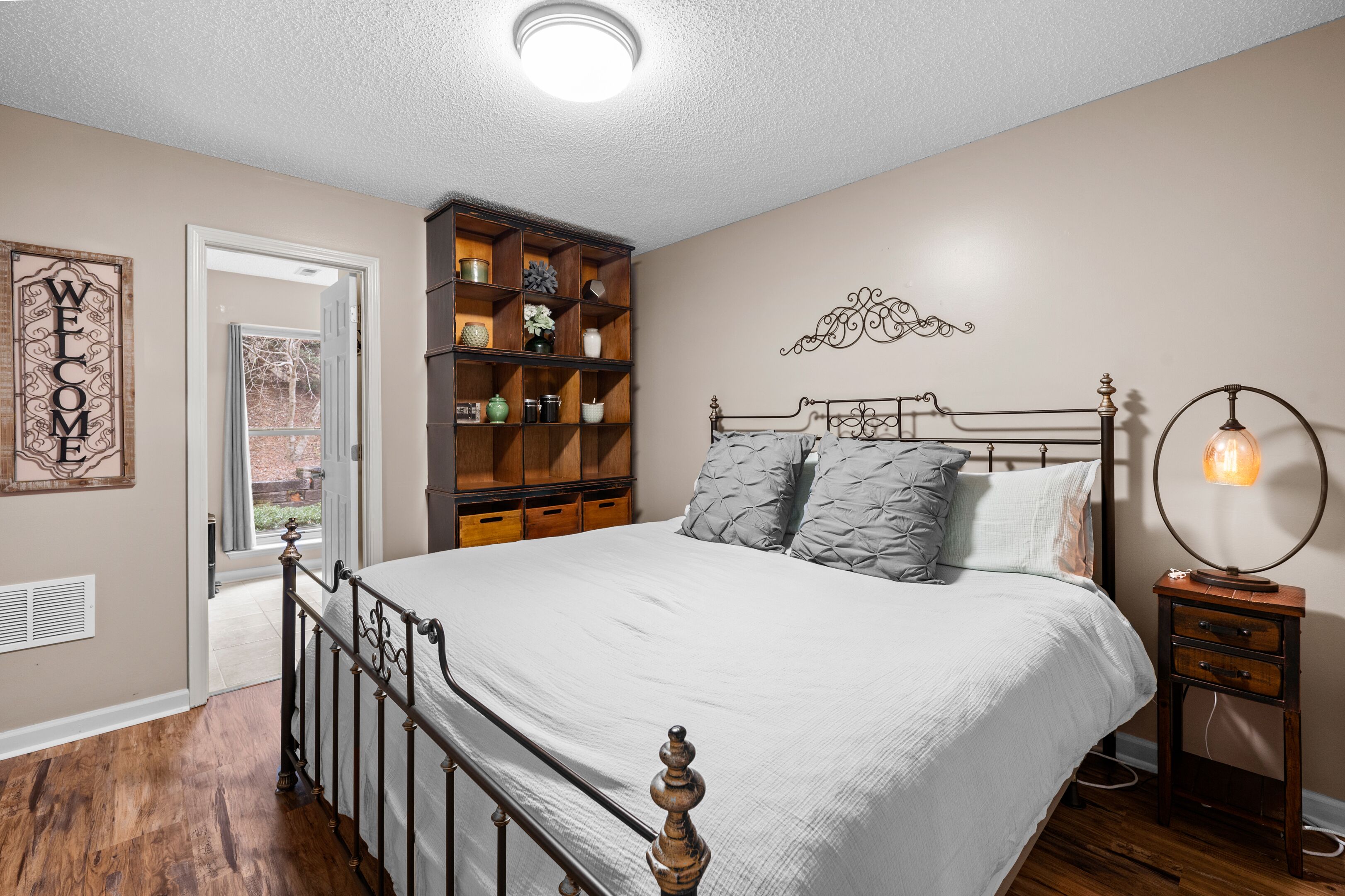 Une chambre à coucher comprenant un lit, une table de chevet, une étagère fixée au mur et une porte donnant sur l’extérieur.