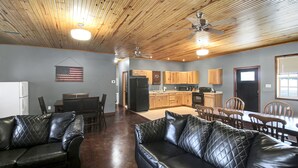 A spacious living area with a black leather sofa, wooden dining table, and kitchen in the background. - Spacious Lodge on 40 Acres! (Cherryvale)