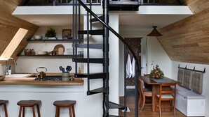 A loft-style kitchen with a central spiral staircase, wooden flooring, and a dining area with a sofa and ottoman.