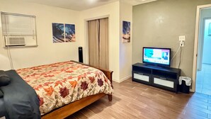 A bedroom with a bed, a television, a ceiling fan, and a window with blinds.