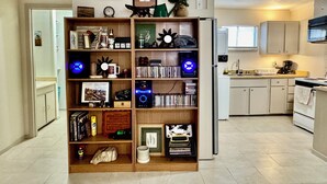 A compact living space with a central bookshelf, a small kitchen area, and a door leading to another room.