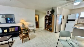 A compact living space with a sofa, chairs, a dining table, a kitchen area with appliances, and a TV.
