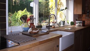 A kitchen with a wooden countertop, a sink, and a window overlooking a garden. - Sandford Meadow Guest House (Oxford)