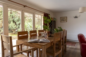 A dining area with a wooden table, chairs, and a view of greenery through large windows. - Sandford Meadow Guest House (Oxford)