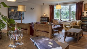 A cozy living room with wooden furniture, a dining table with wine glasses, and a large window with curtains. - Sandford Meadow Guest House (Oxford)