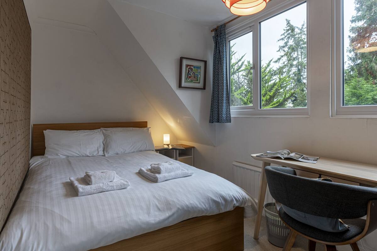 A bedroom with a bed, bedside table, chair, and a window with a view of trees.