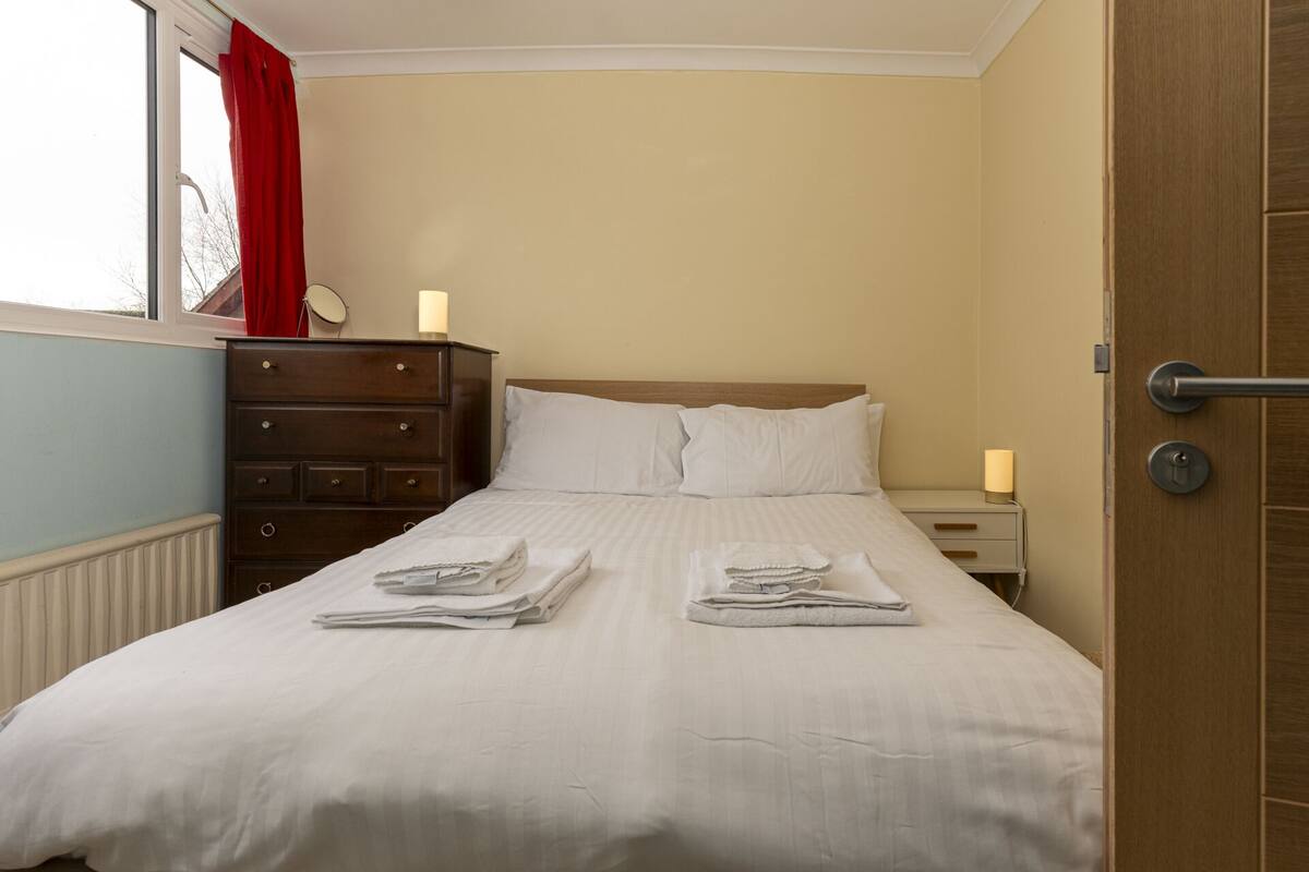 A neatly made bed with folded towels, a wooden dresser, and a nightstand with a lamp.