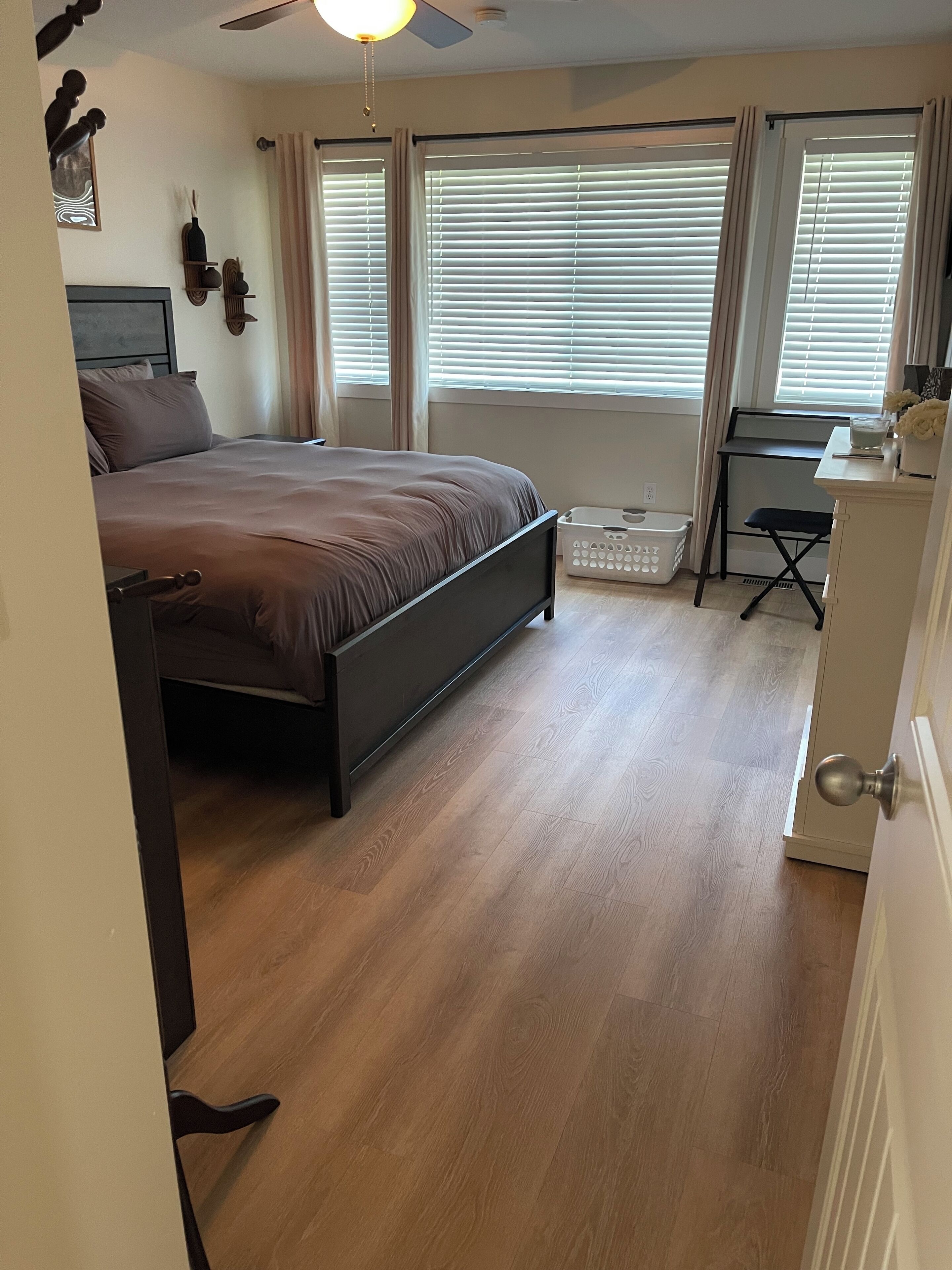 A bedroom with a bed, a desk, a chair, a ceiling fan, and a window with blinds.