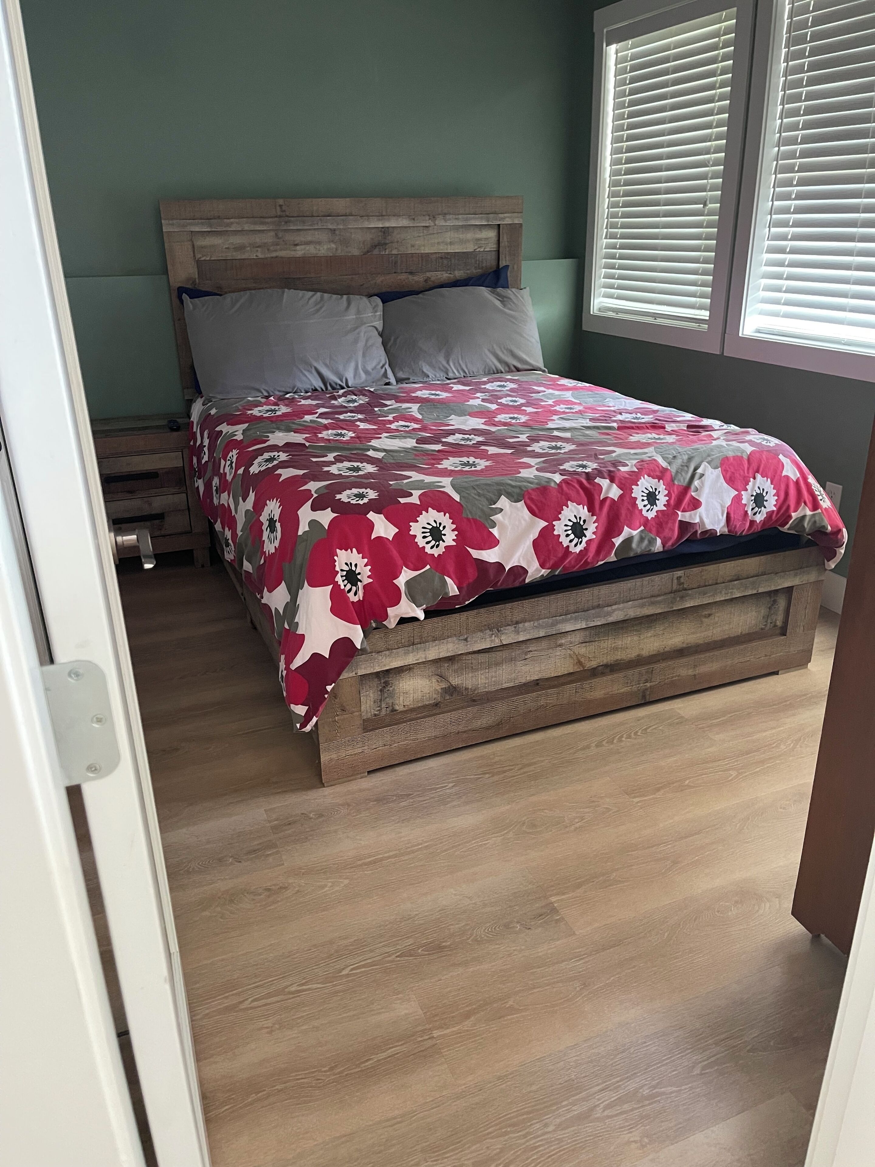 A bed with a floral bedspread, a wooden headboard, and a window with blinds.