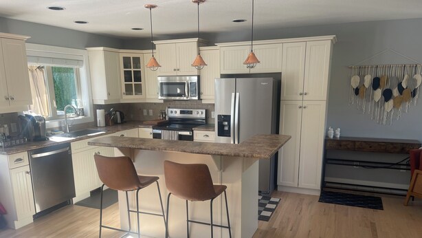 A modern kitchen with white cabinets, a central island with bar stools, stainless steel appliances, and pendant lighting.