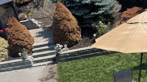 A patio area with a glass table and chairs, a pool, and a lawn.