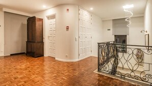 A spacious room with wooden flooring, a dark wooden cabinet, white doors, and a metal staircase railing.