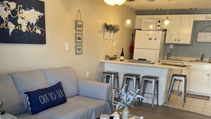 Ein modernes Wohnzimmer mit grauem Sofa, einem Zierkissen, einer weißen Kommode und einem gemusterten Teppich.