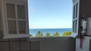A kitchen with a gas stove, a window with a view of the ocean, and a tiled backsplash. - Feet in the water 2 (Les Anses-d'Arlets)
