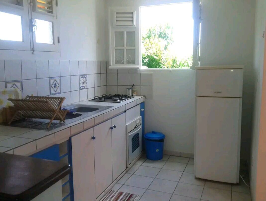 A compact kitchen with a gas stove, a sink, a small oven, and a refrigerator. There is a window providing natural light and a view of greenery outside.