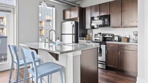 A modern kitchen with a central island, stainless steel appliances, and wooden cabinets. - The Residences at CityWay (Indianapolis)